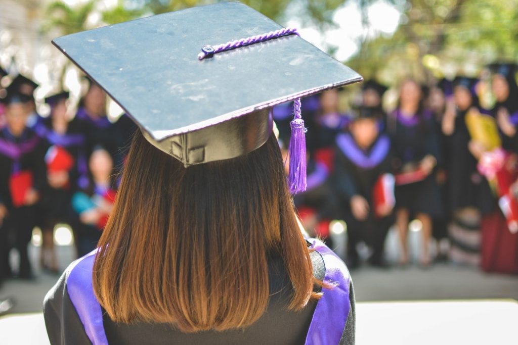 Image of a girl's back, with short brown hair and wearing a black graduation cap and purple robes, inserted in a post about how to invest 100 dollars